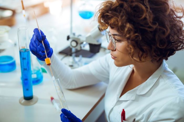 Como é feito o exame toxicológico: mulher em laboratório analisando amostra em tubo.