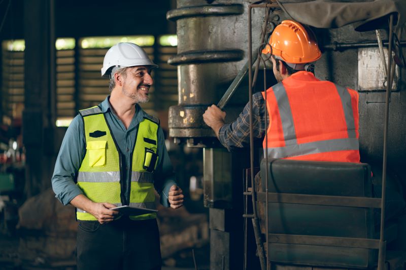 Técnico dando dicas de segurança no trabalho ao profissional, ambos utilizando EPIs.