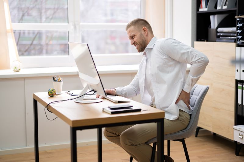 NR-17 atualizada: homem no escritório se contorcendo com dor nas costas devido à postura incorreta.