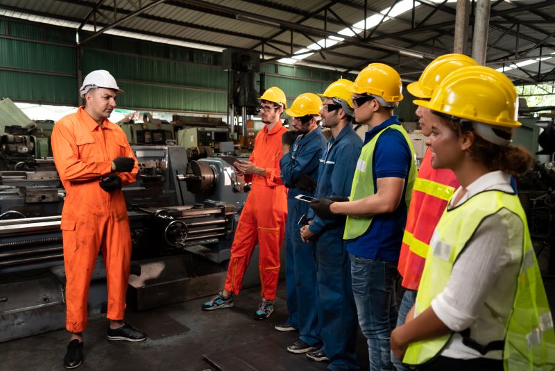 Profissionais capacitados: engenheiro ministrando treinamento a funcionários em indústria, todos vestindo EPIs.