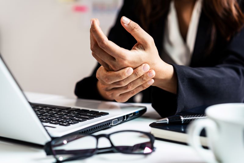 DORT e LER: close de mulher massageando o pulso enquanto trabalha no computador.