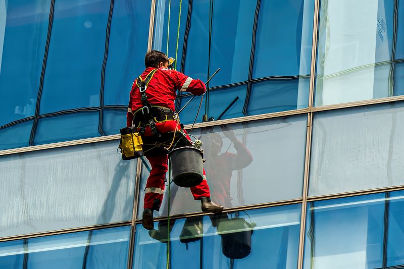 periculosidade o que é​: homem limpando vidros em altura pendurado com EPIs