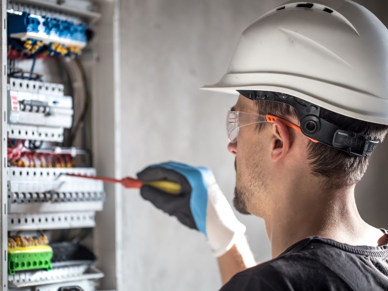 riscos ocupacionais​: eletricista trabalhando em caixa de energia e vestindo EPIs